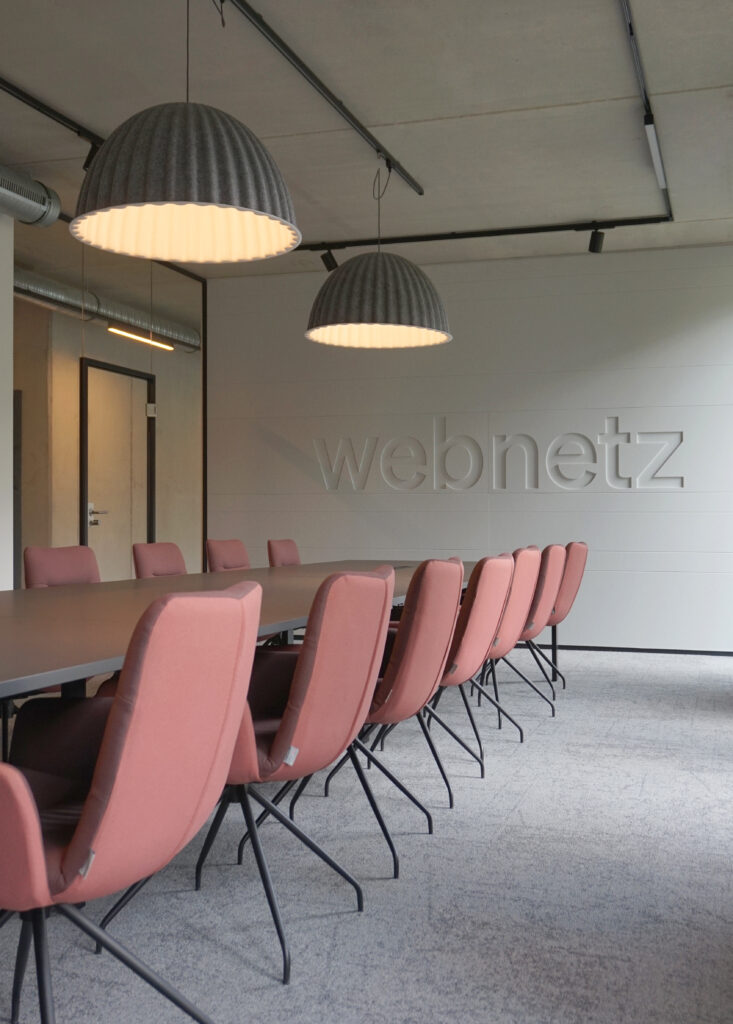 Konferenzraum mit roten Stühlen und eingefrästem Logo an grauer Akustikwand