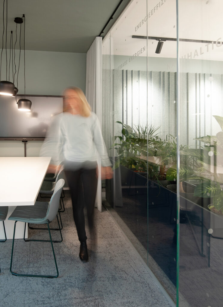 Konferenzraum mit grüner Decke und seitlicher Glaswand mit dahinter liegenden Pflanzengefäßen