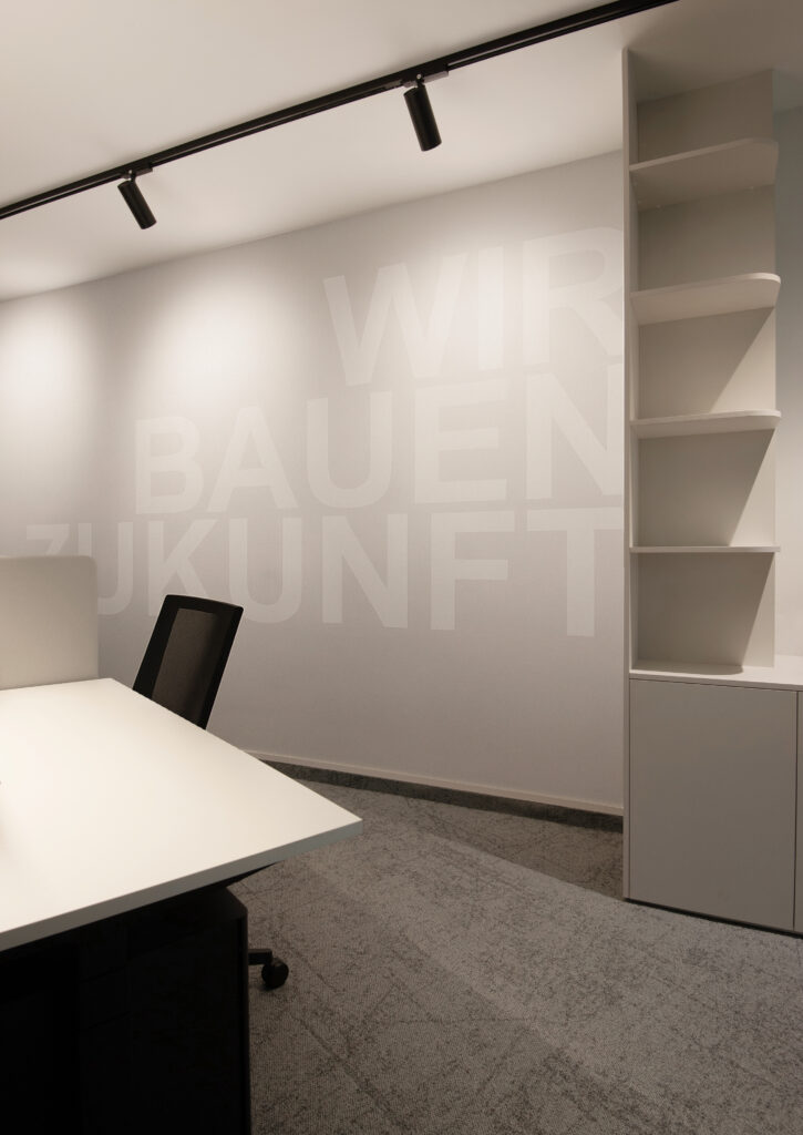 Graue Bürowand mit weißer Schriftzug und offenem Regal