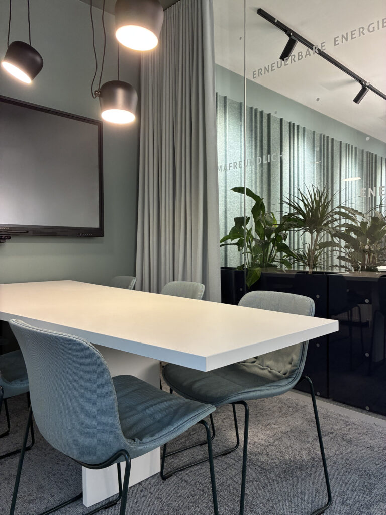 gläserner Konferenzraum mit weißem Tisch und schwarzen Pendelleuchten