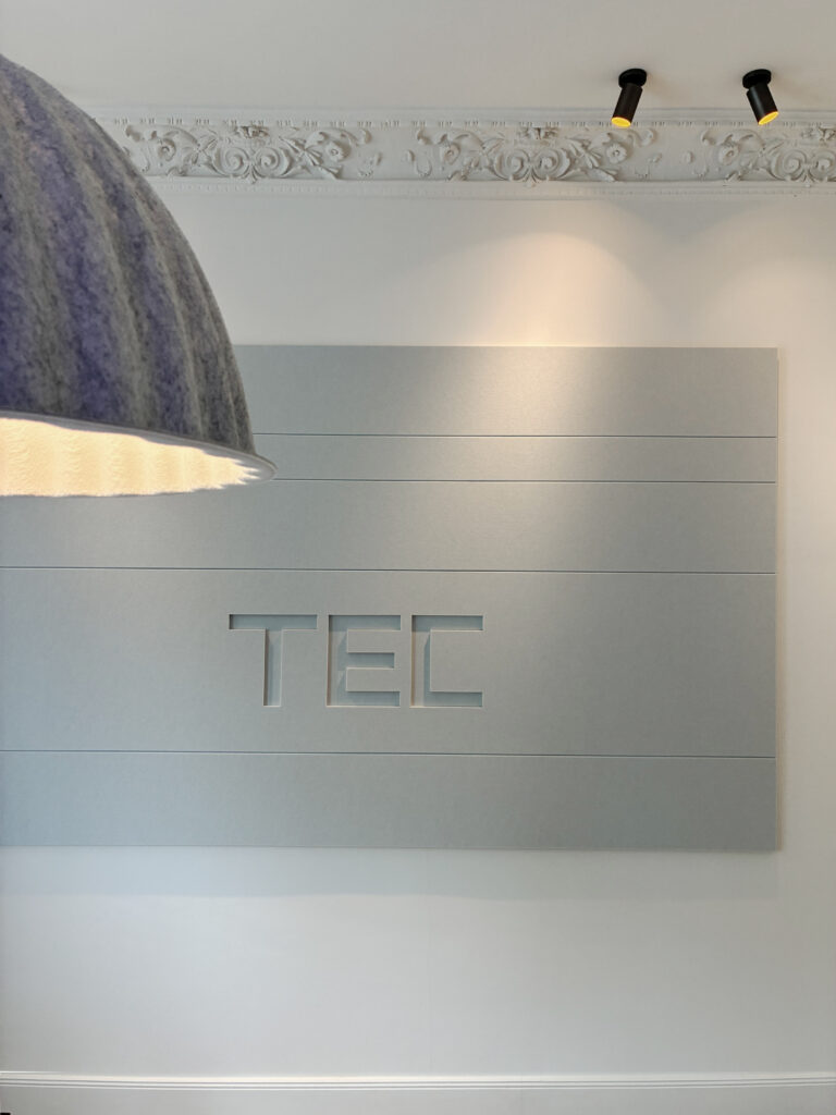 Wandabsorber mit ausgestanztem Logo und Pendelleuchte davor.