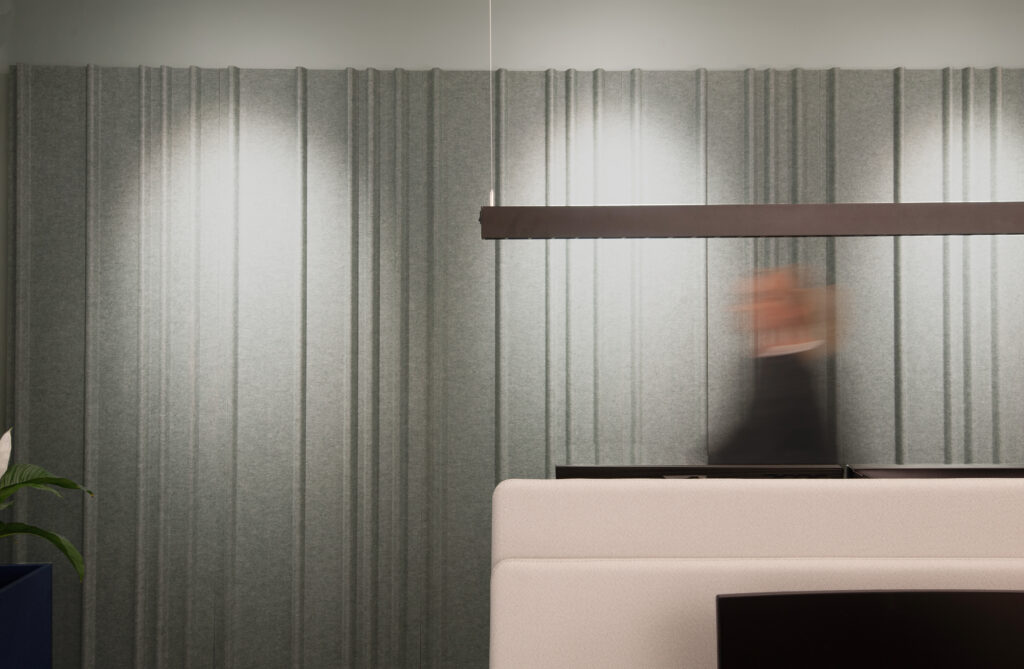 Akustische Wandbekleidung in der Farbe Grün mit schwarzer Pendelleuchte und Tischtrennwänden an Schreibtischen