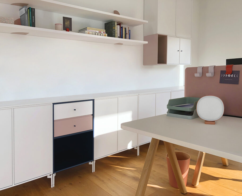 Büroraum mit Schreibtisch, einem Sideboard in den Farben Blau, Weiß und Rosa sowie weißem Wandregal