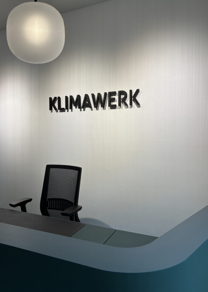 Grüner Empfangstresen mit schwarzem Bürostuhl und Logo auf Streifentapete